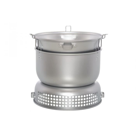 Retkikeitinsetti pakattuna kompaktiksi kokonaisuudeksi, kattilat ja paistinpannu sisäkkäin tuulisuojassa.